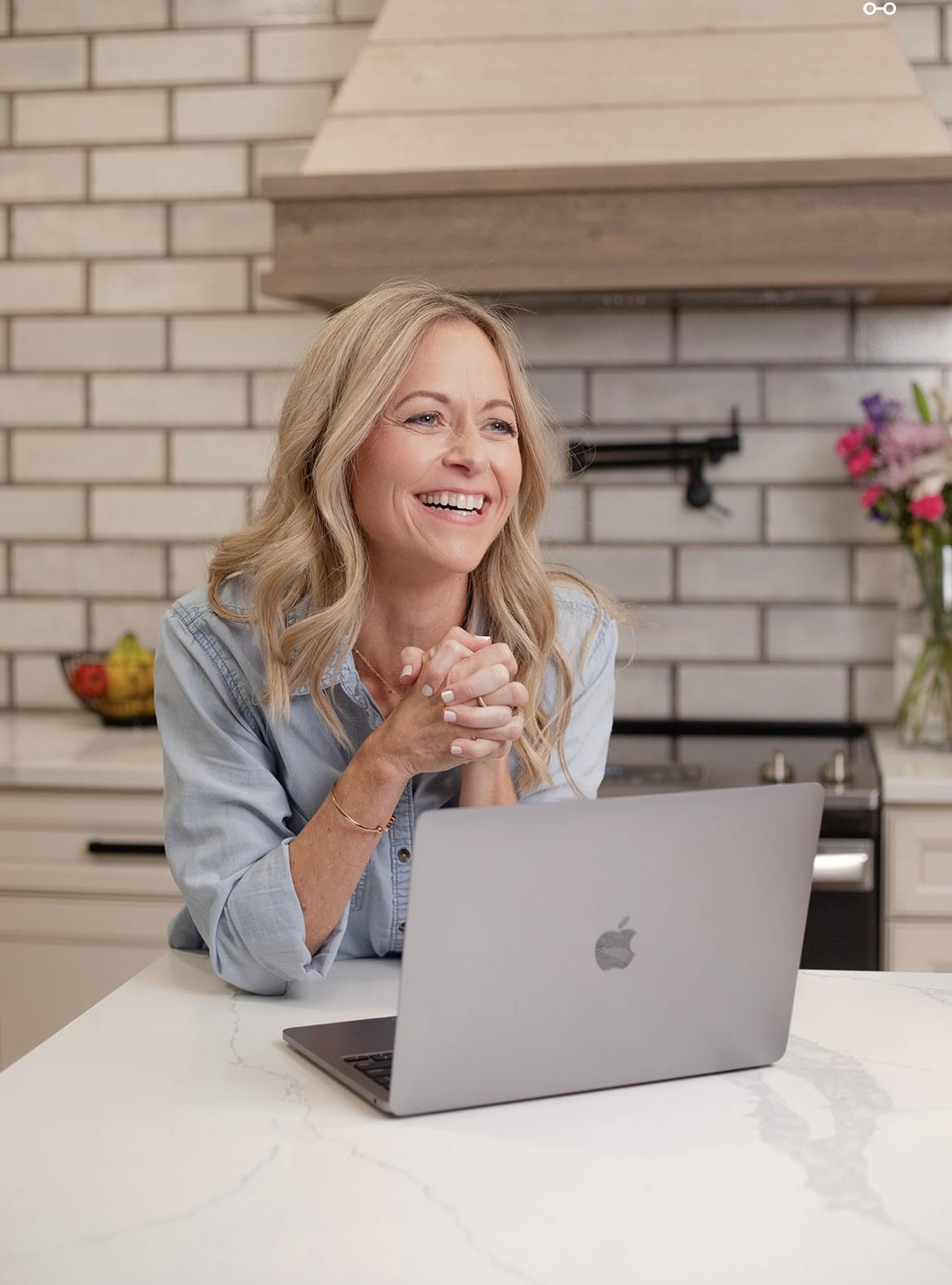 Erin Blair smiling at her kitchen counter with her laptop